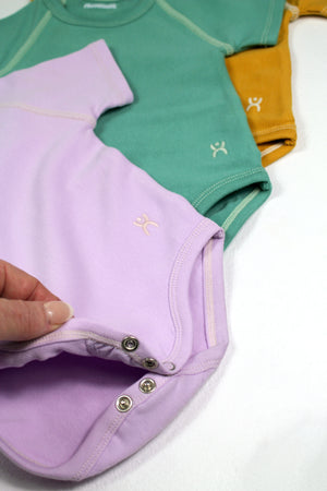 Flexisuit lavender bodysuit featuring a fitted design with long sleeves and a scoop neckline, displayed on a mannequin.